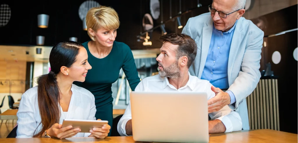 Geschäftsleute unterschiedlichen Alters um einen Laptop versammelt